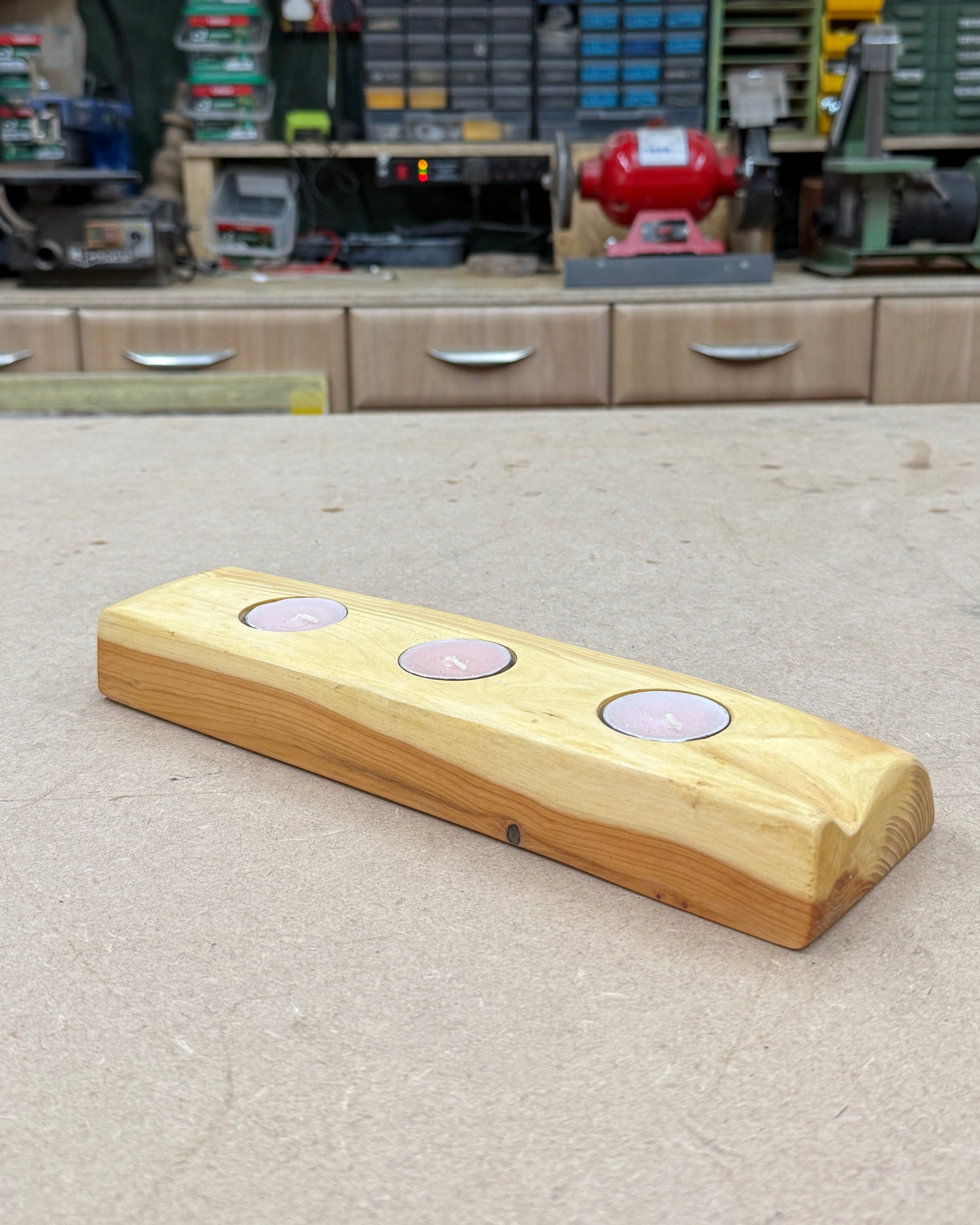 Wooden candle holder with three tea lights on a concrete top in a workshop setting.