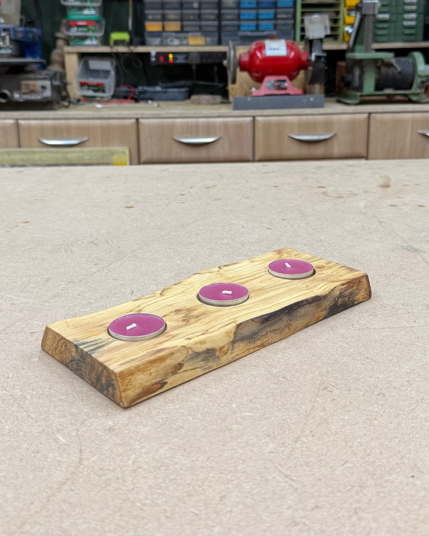 Wooden candle holder with purple tea lights on a concrete top in a workshop.