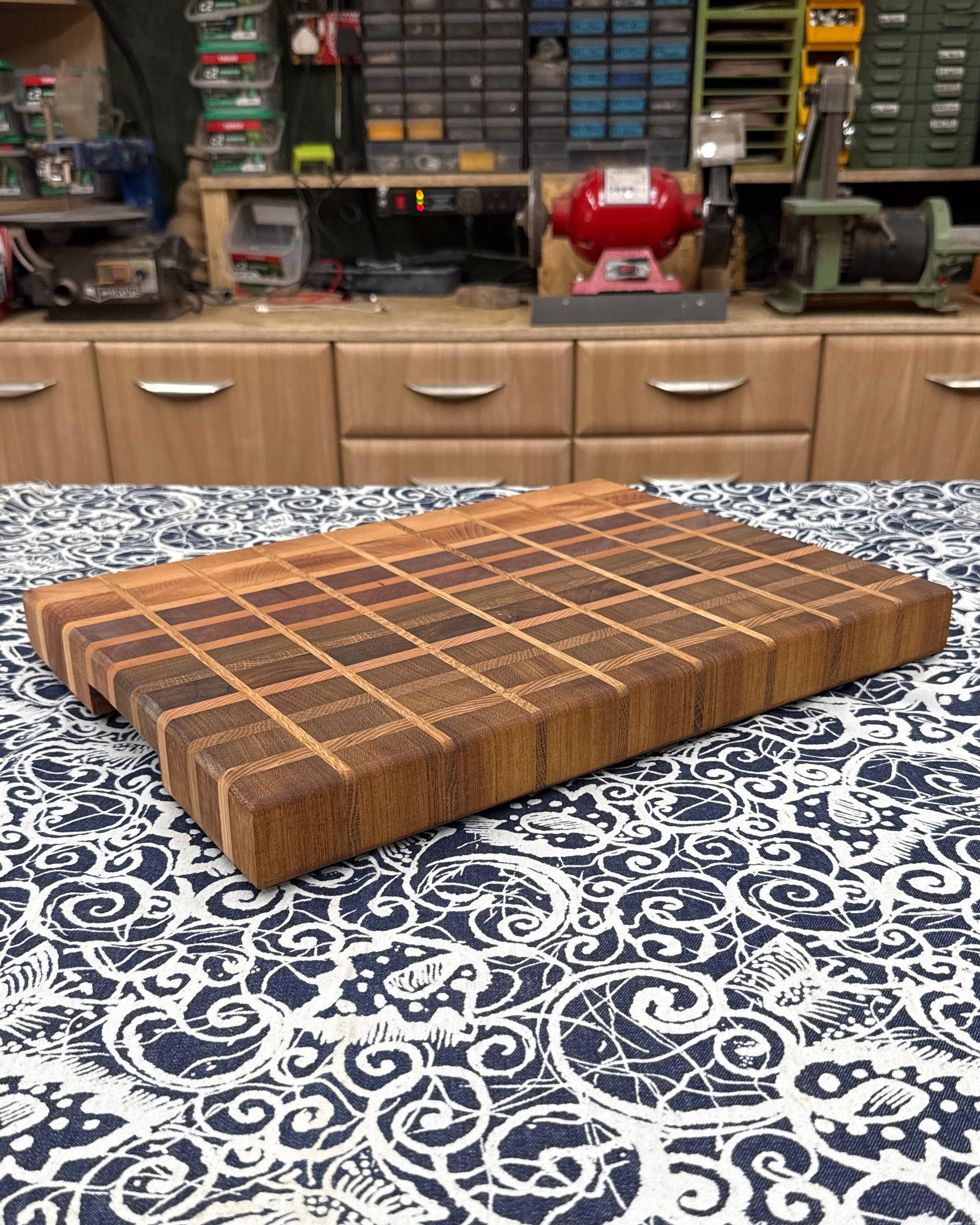 Wooden cutting board on a patterned tablecloth with shelves and storage units in the background