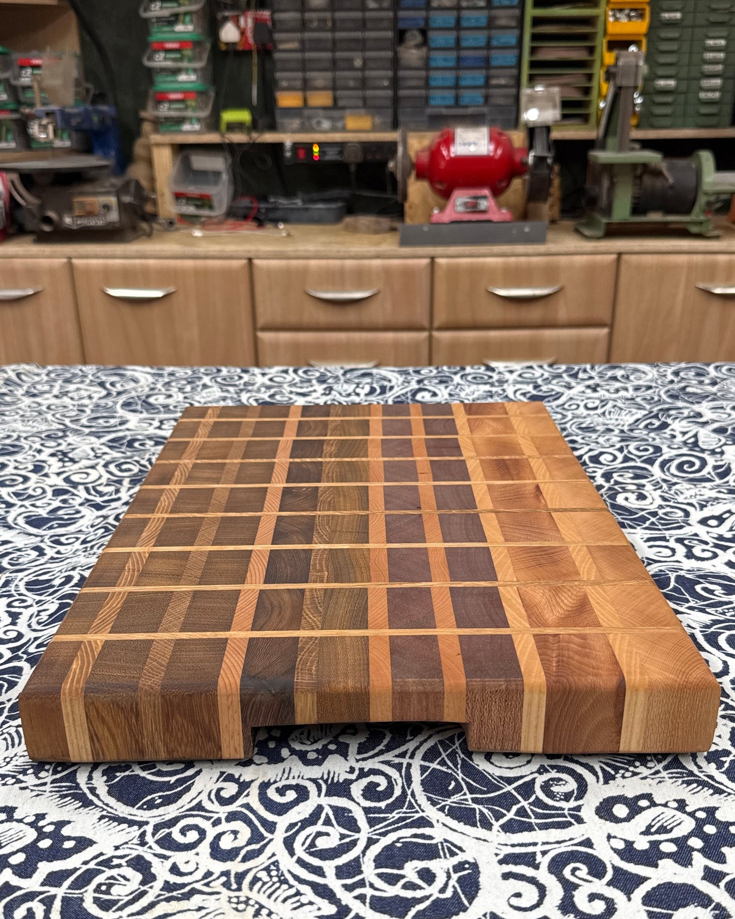 Wooden cutting board on a patterned tablecloth with a workshop in the background