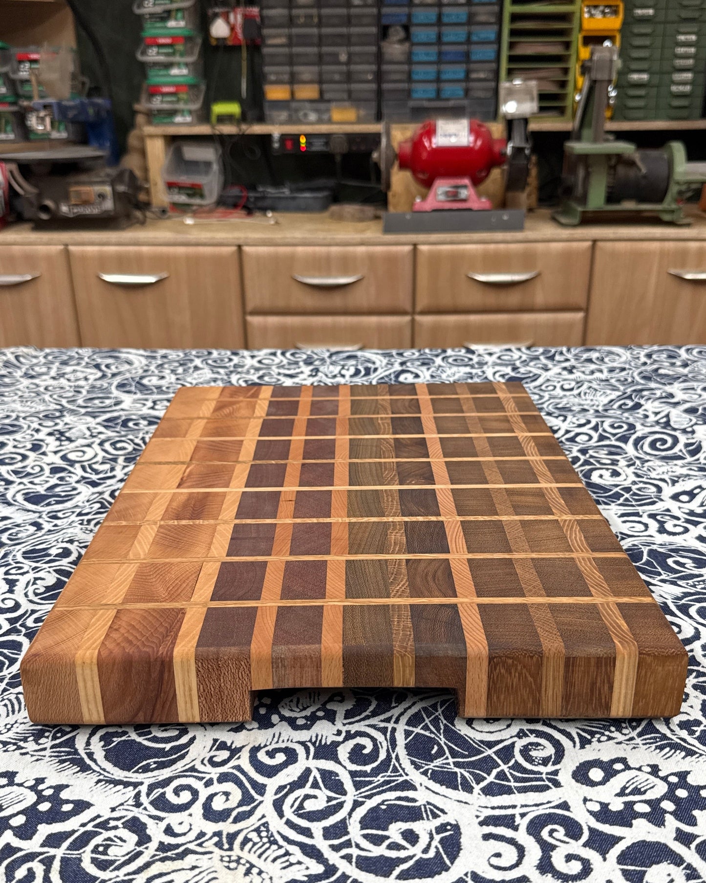 Wooden cutting board on a patterned surface with a workshop in the background