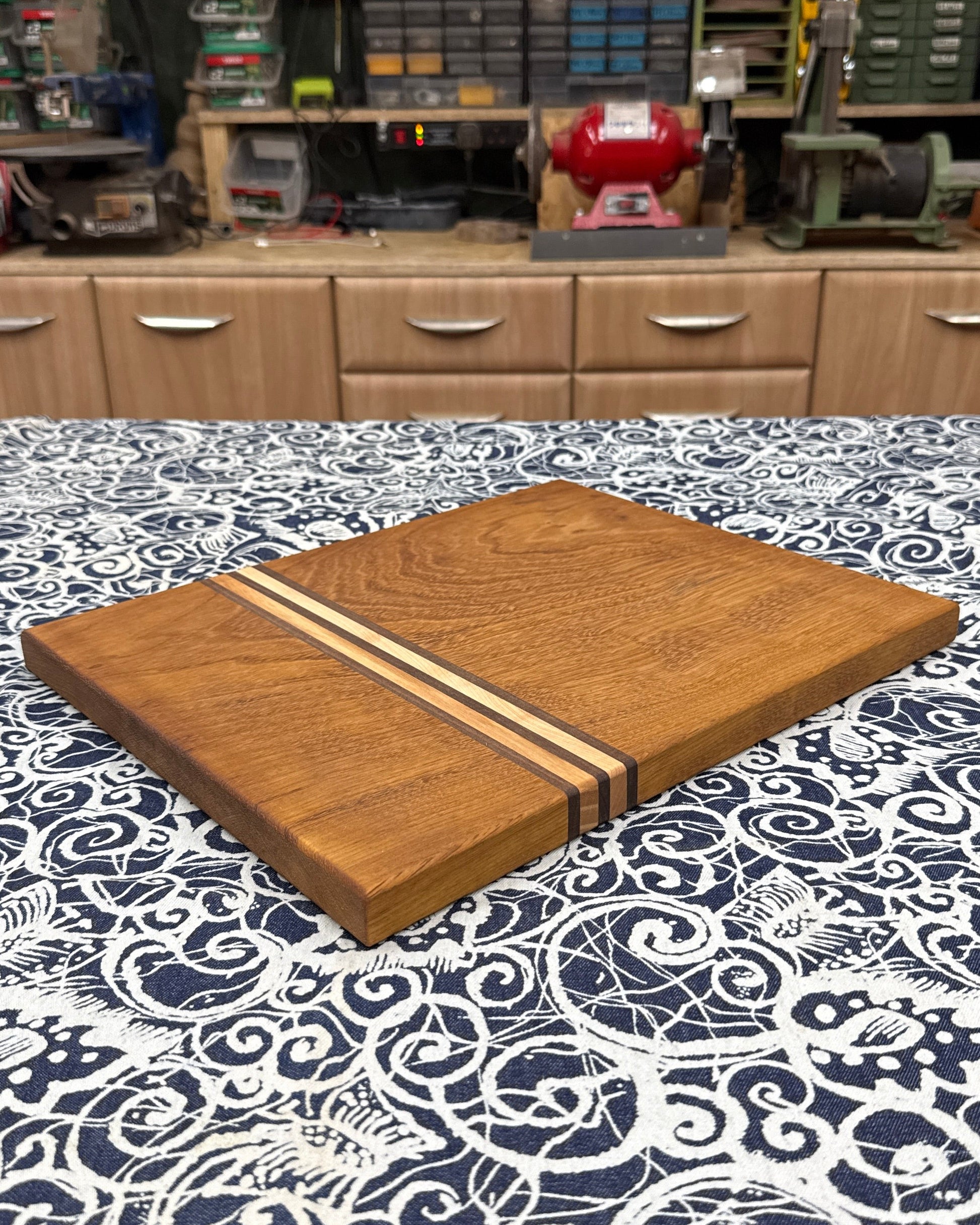 Wooden cutting board with a striped design on a patterned tablecloth in a workshop setting.