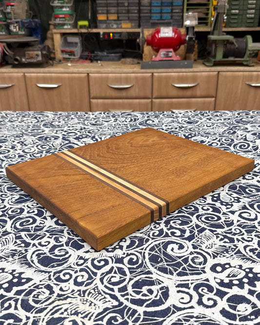 Wooden cutting board with a striped design on a patterned tablecloth in a workshop setting.