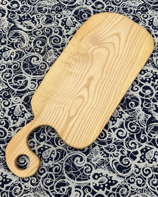 Wooden charcuterie board with handle on a patterned fabric background