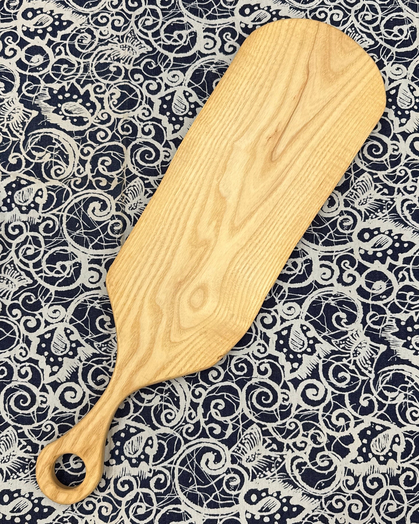 Wooden charcuterie paddle on a patterned fabric background