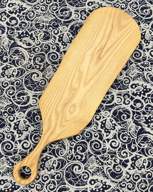 Wooden charcuterie paddle on a patterned fabric background